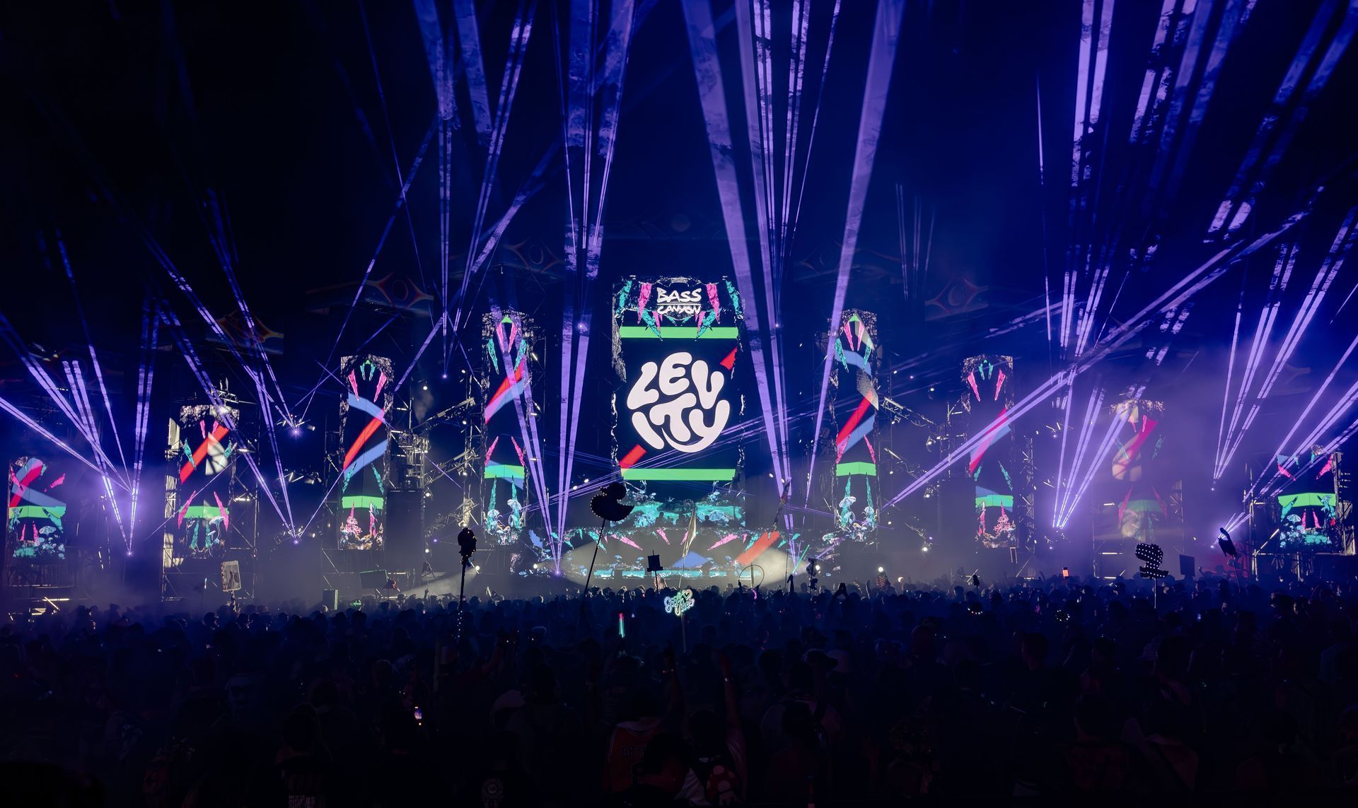 A vibrant EDM concert stage with bright lights and crowd, mainly blue and purple colors.