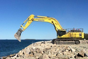 Yellow Komatsu Excavator on Rocks by the Blue Ocean — CJD Investments (NQ) Pty Ltd in Mackay Harbour, QLD