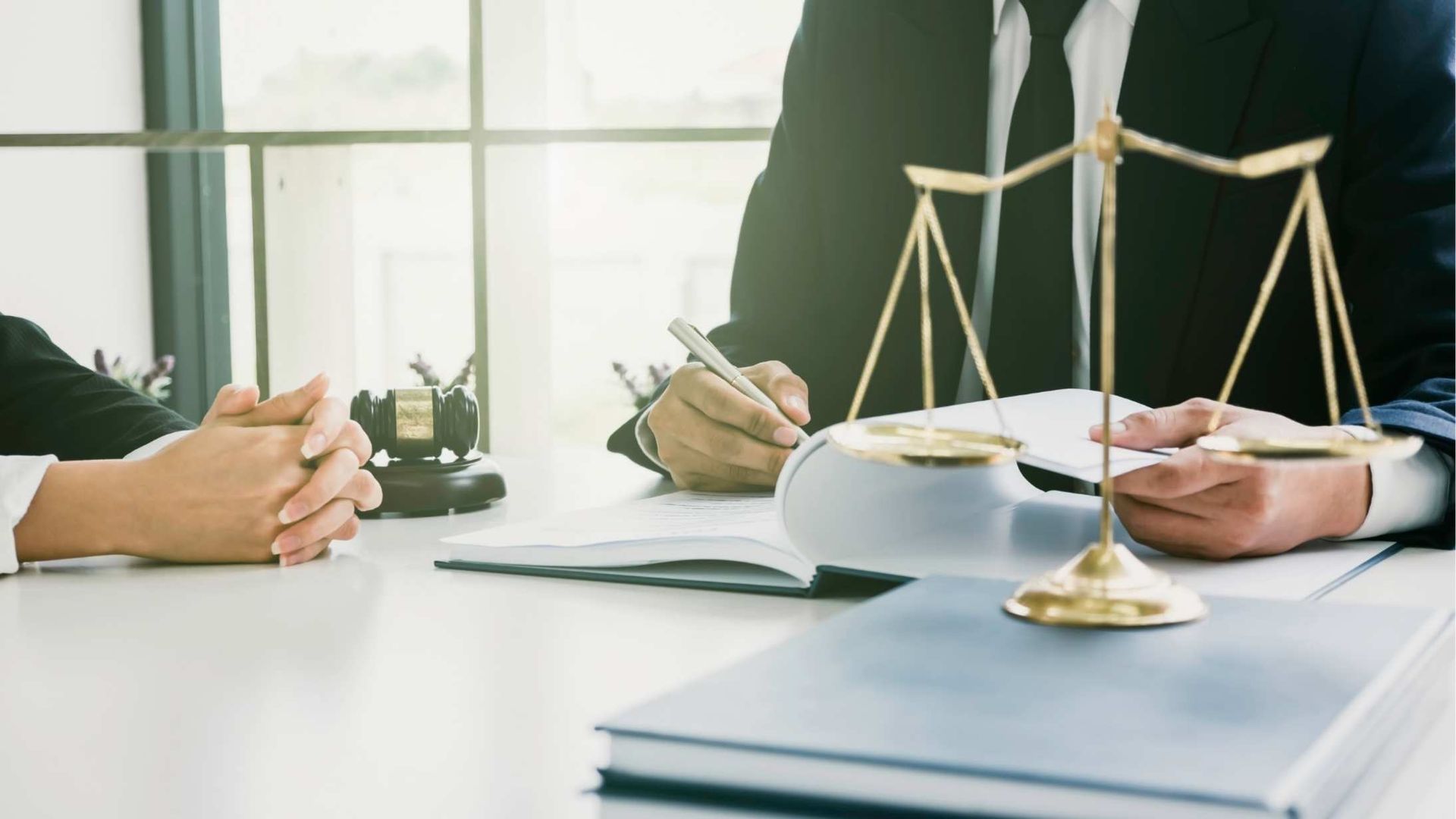 Lawyer in suit reviewing documents with client, scales of justice on desk.