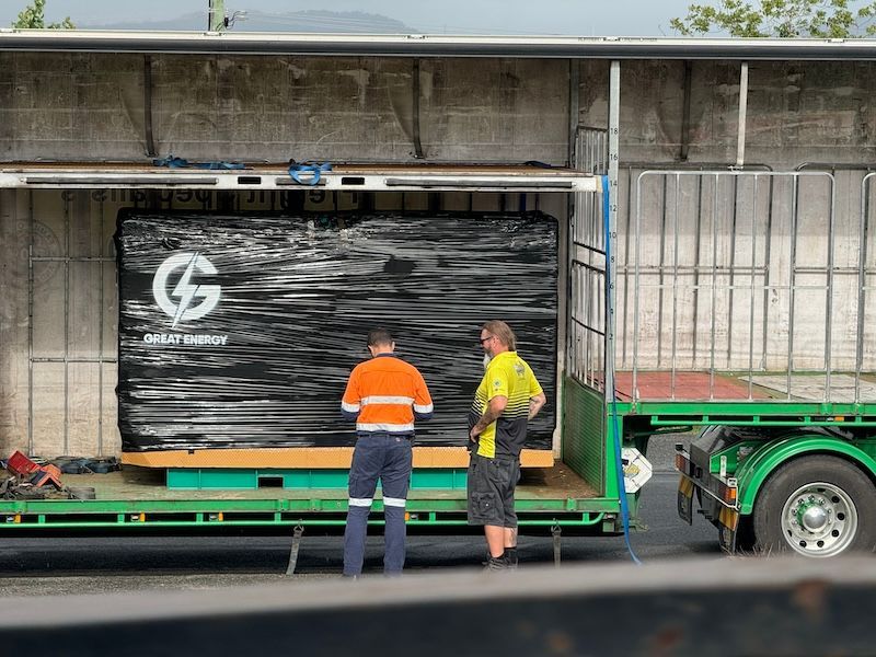 Two Workers By A Truck Transporting A Large, Black, Wrapped Item Labeled — Great Energy in Portsmith, QLD