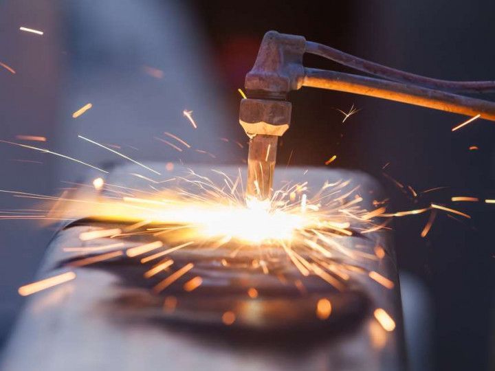 A metal cutting torch directs a bright flame onto a piece of metal, creating a spray of glowing sparks.