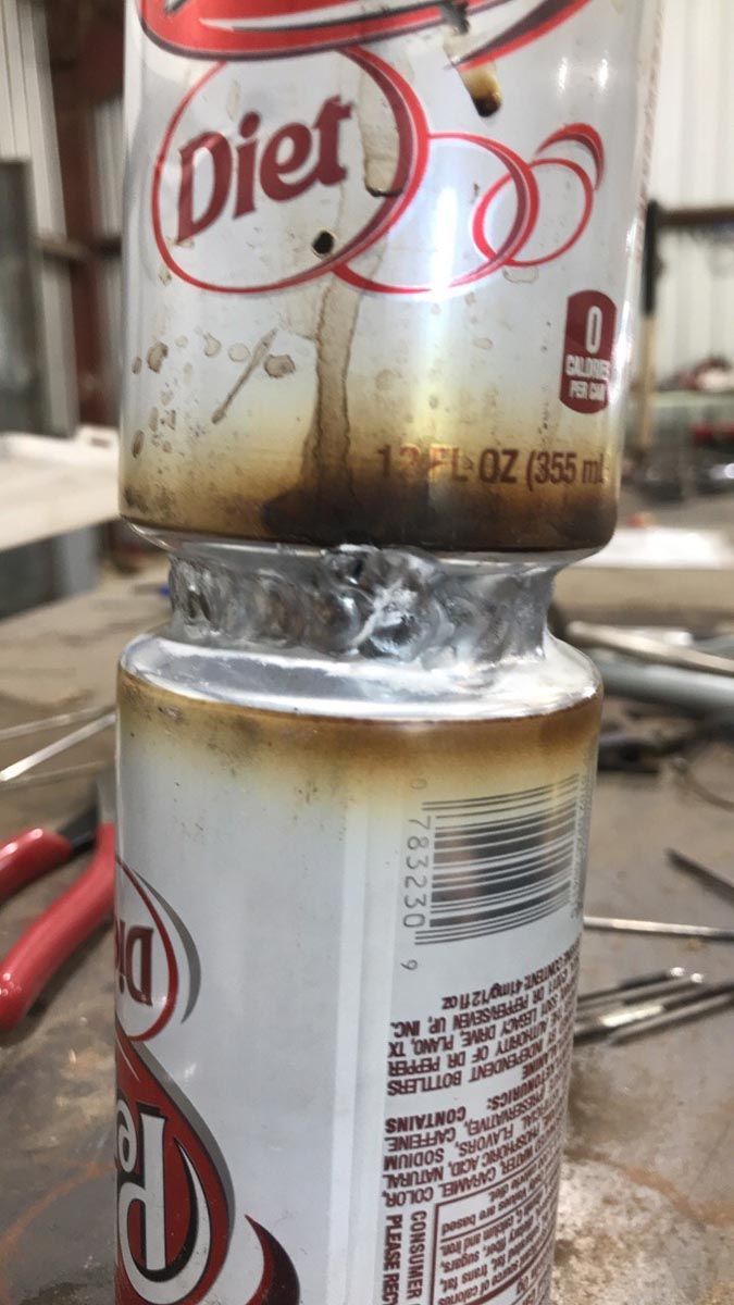 Two Diet Dr Pepper soda cans are stacked vertically, joined together with a silver, uneven welded seam in the middle.