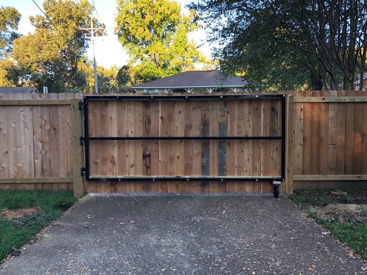 A wood gate with a black metal frame and a small wheel on the bottom right corner, installed in a residential fence.