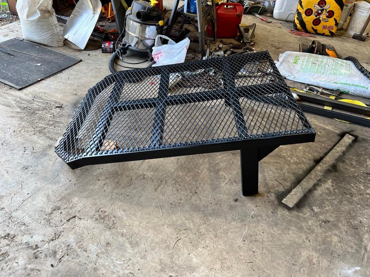 A black, rectangular metal mesh rack with a single support leg resting on a concrete garage floor.