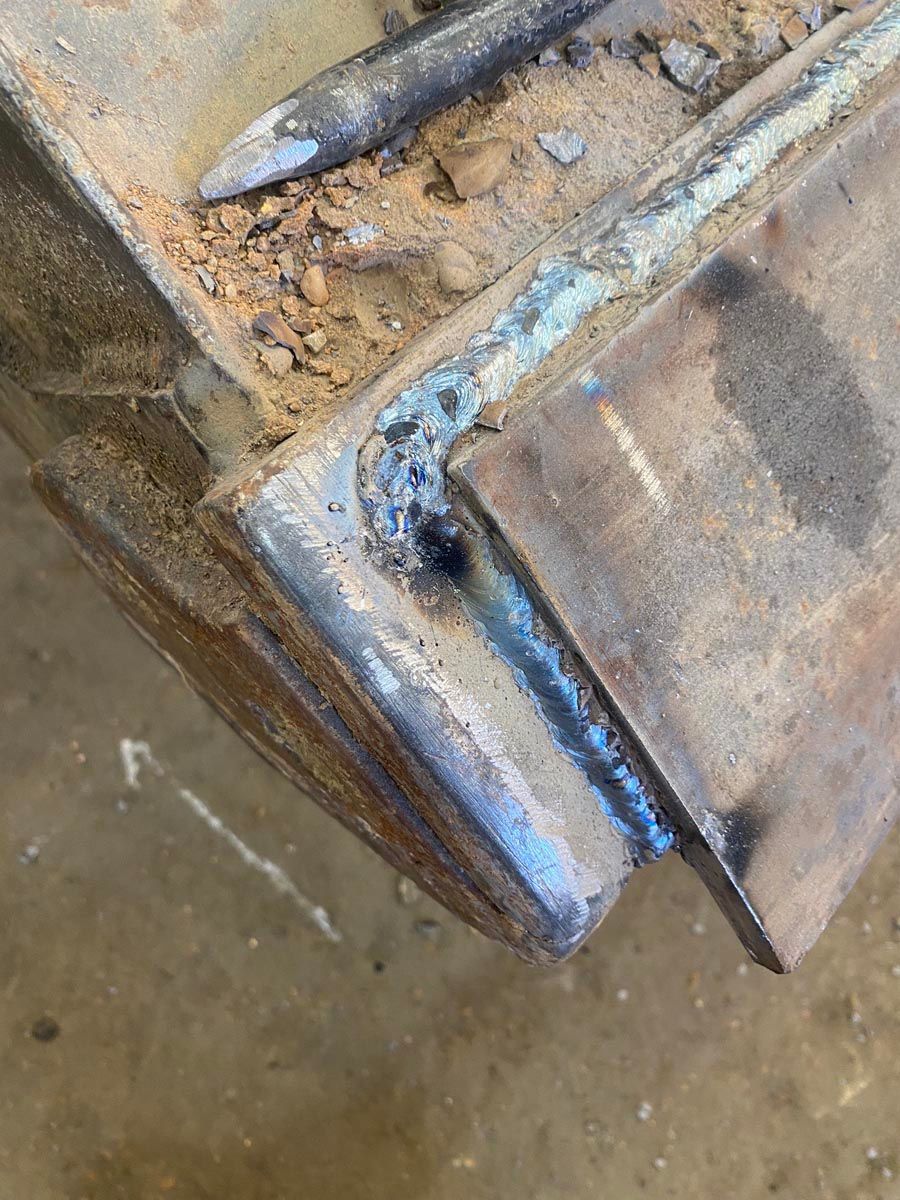 Close-up of a weld bead connecting a thick steel plate to an excavator bucket edge.