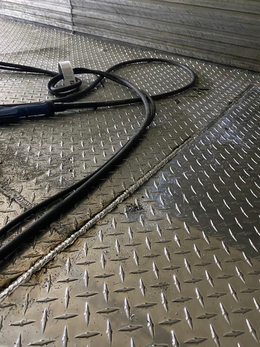 A black power cable lies coiled on a silver diamond-plate metal floor next to a welded metal seam.