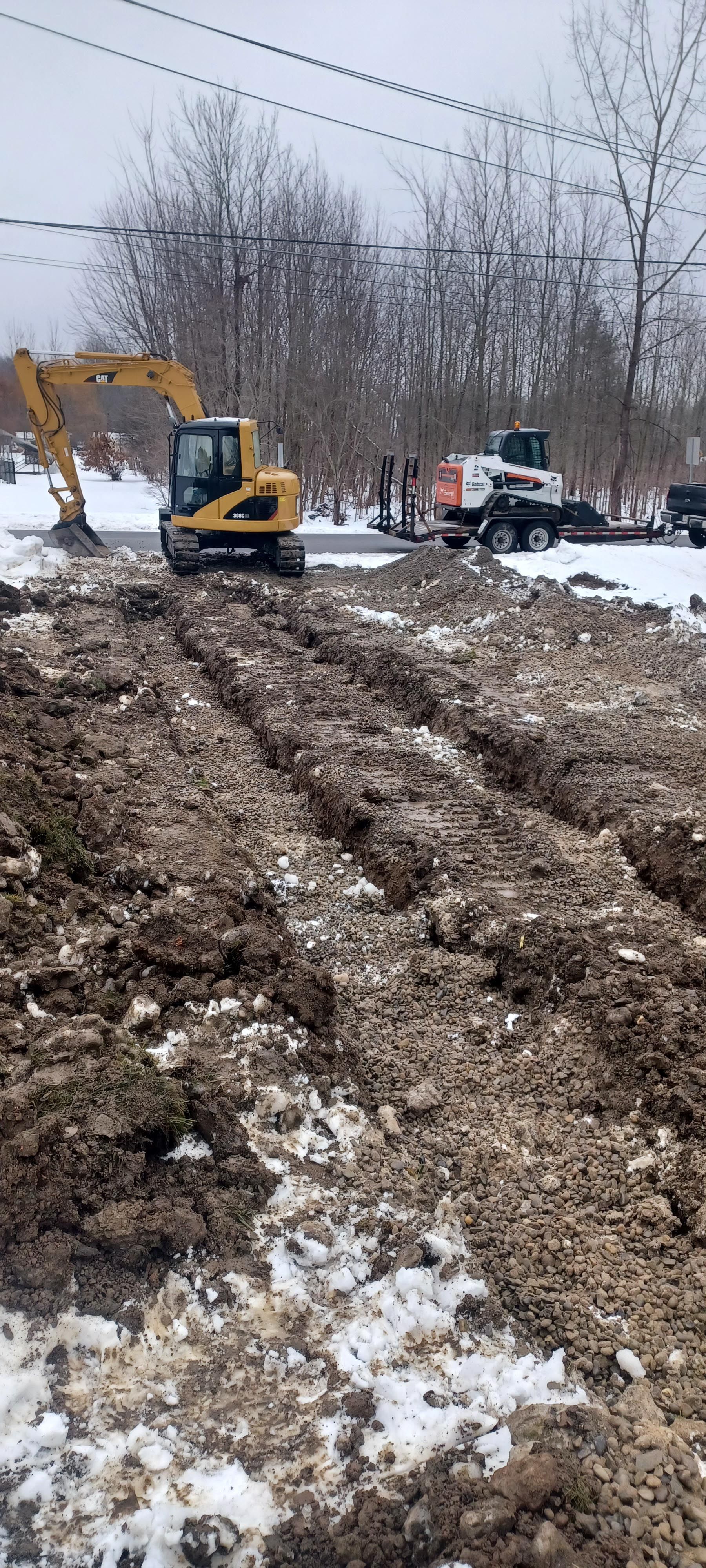 A yellow excavator is moving dirt in a snowy field.