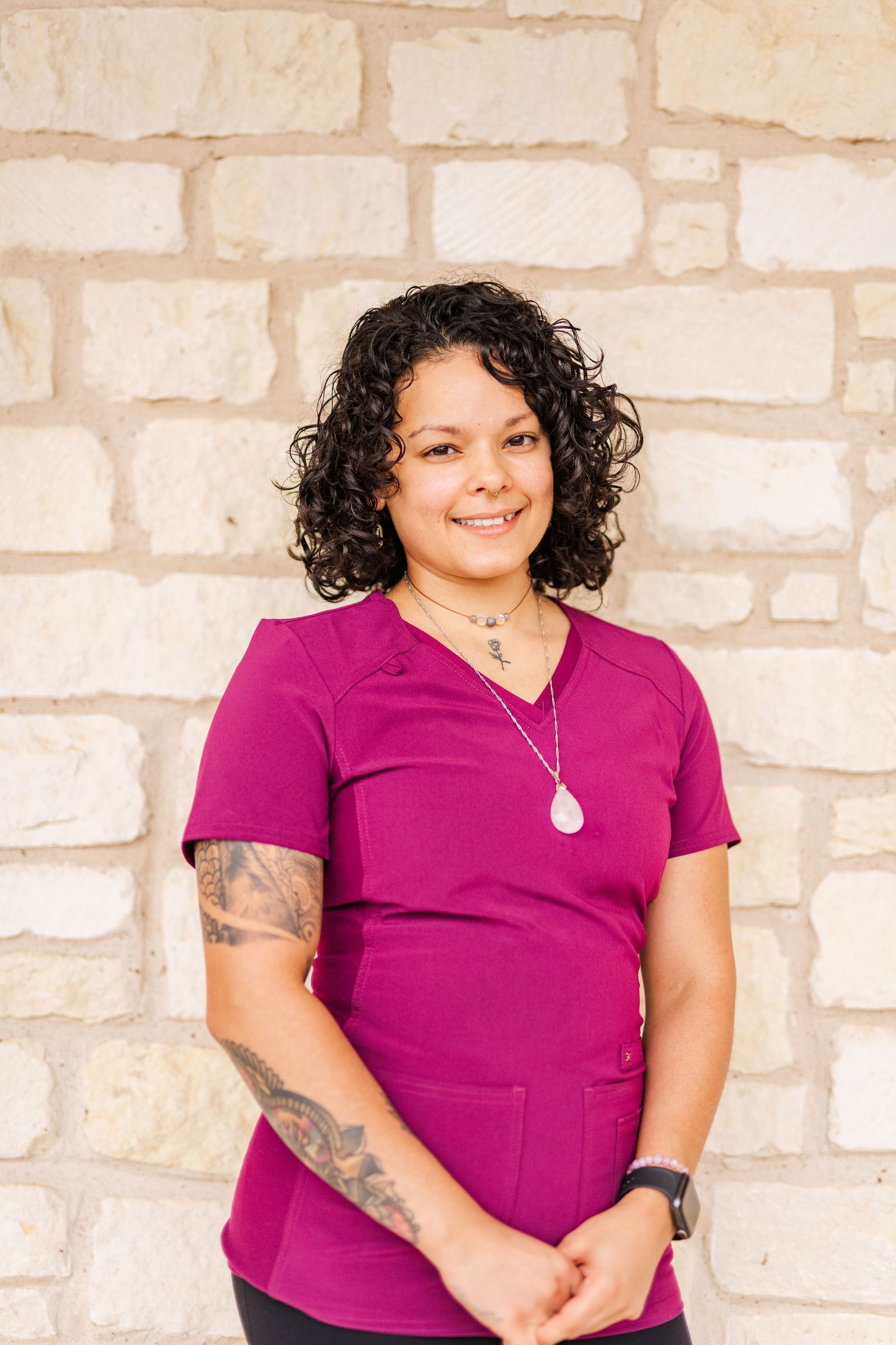A woman in a purple scrub top is standing in front of a stone wall.