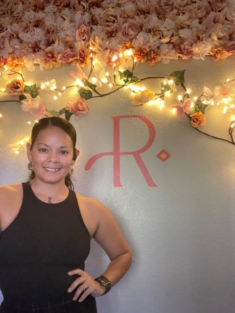 A woman stands in front of a wall with flowers and a letter r.