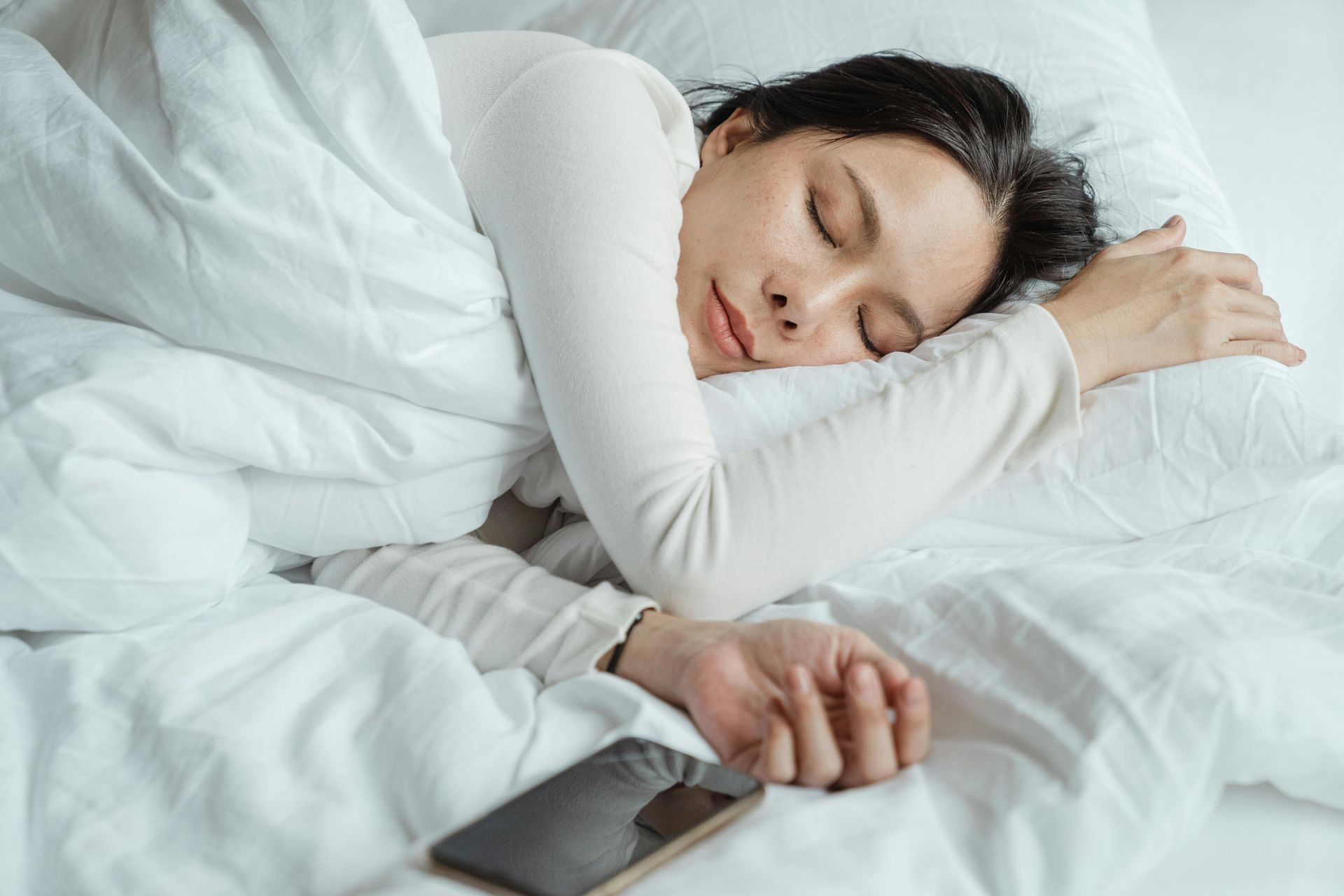 A woman is sleeping in bed with a cell phone next to her.