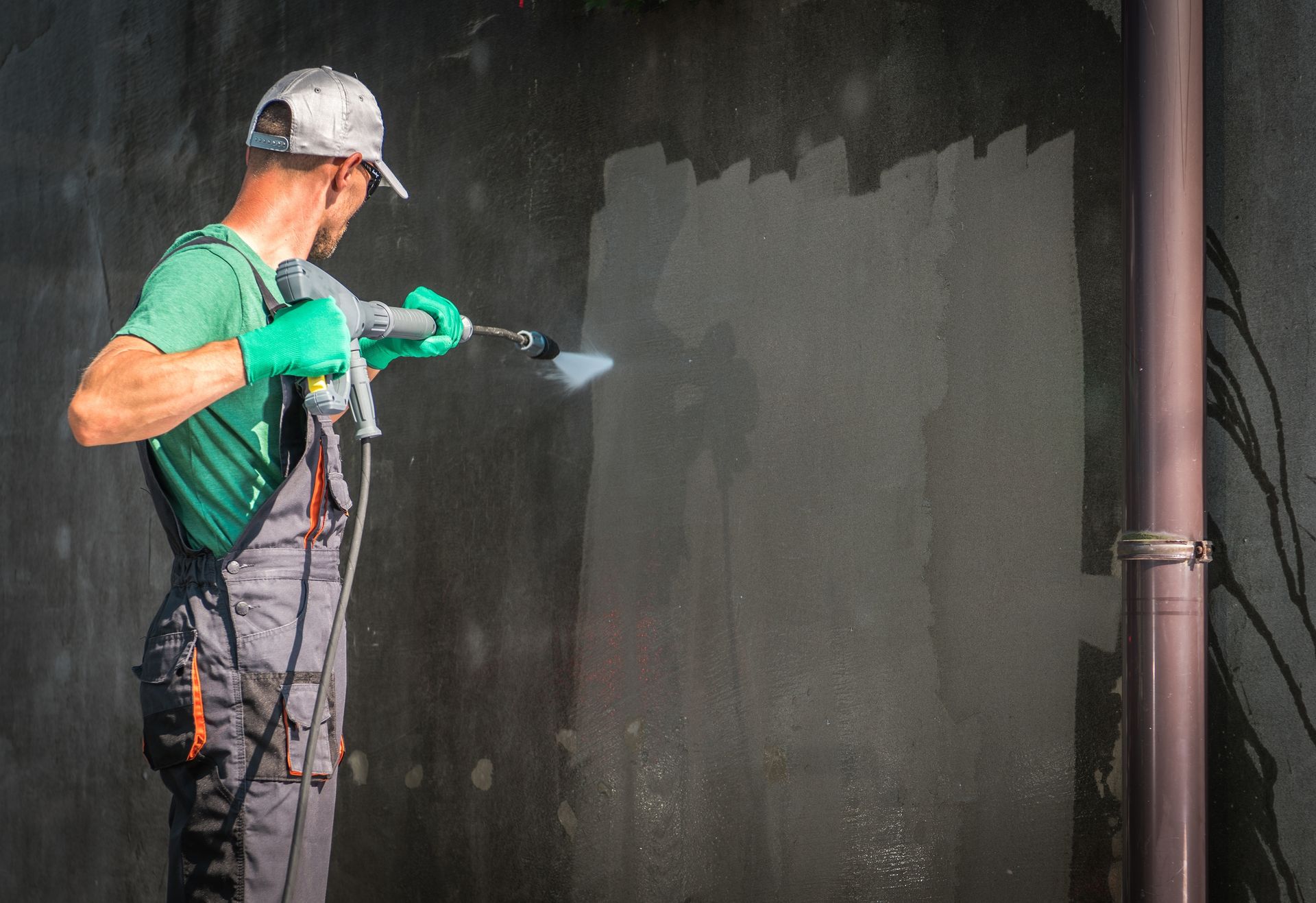 A man is cleaning a wall with a high pressure washer.
