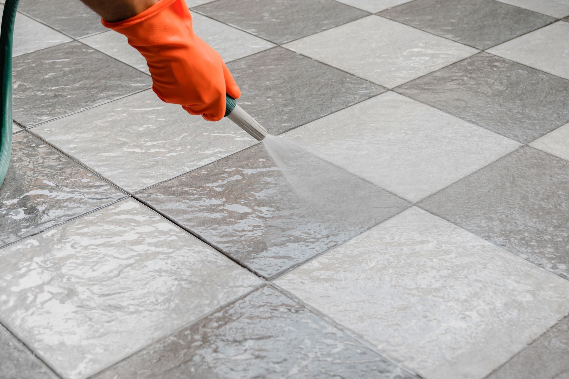 A person is cleaning a tile floor with a hose.