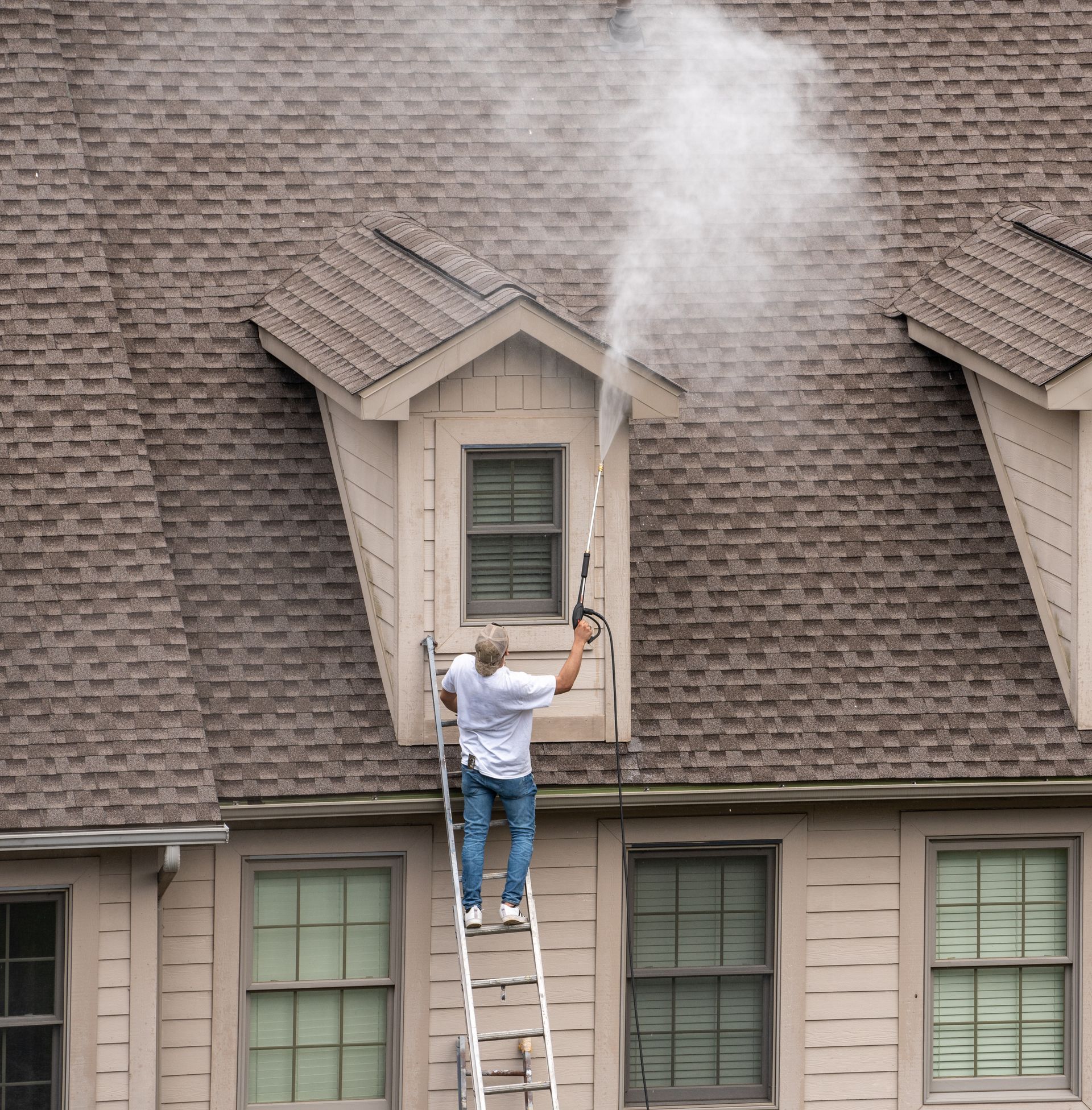 A man on a ladder is cleaning the roof of a house