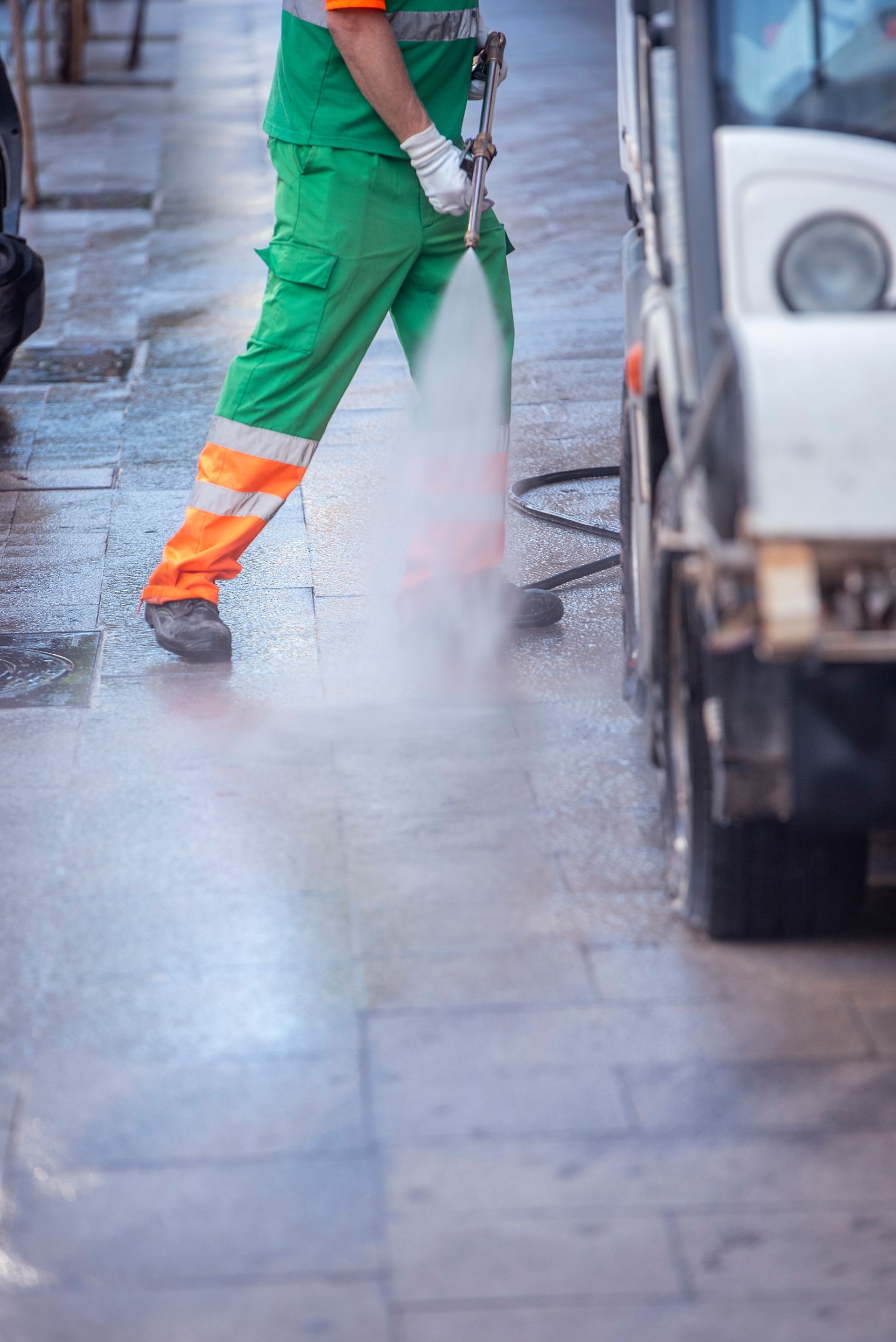 A man is cleaning the sidewalk with a high pressure washer.