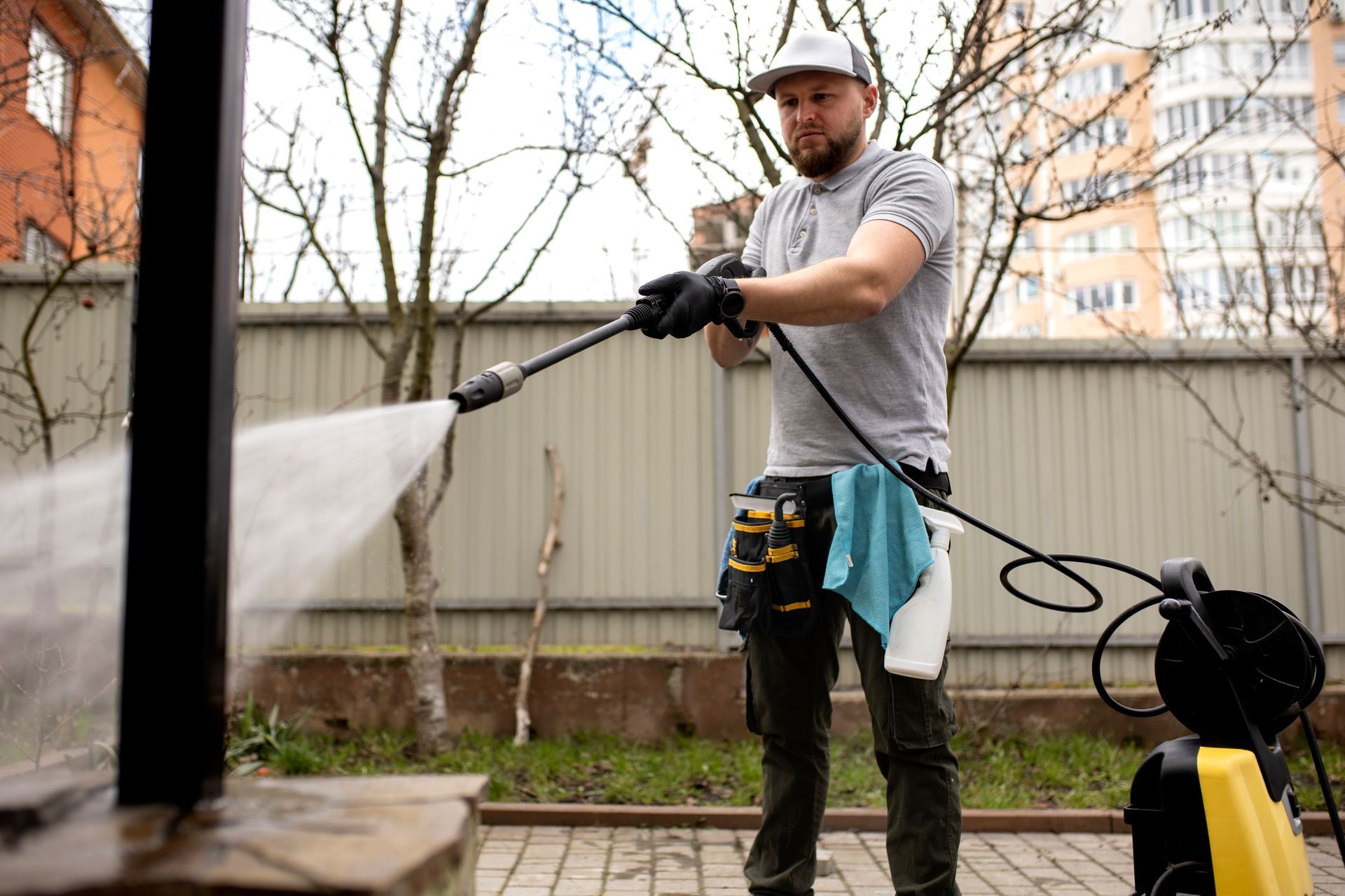 A man is using a high pressure washer to clean a fence.