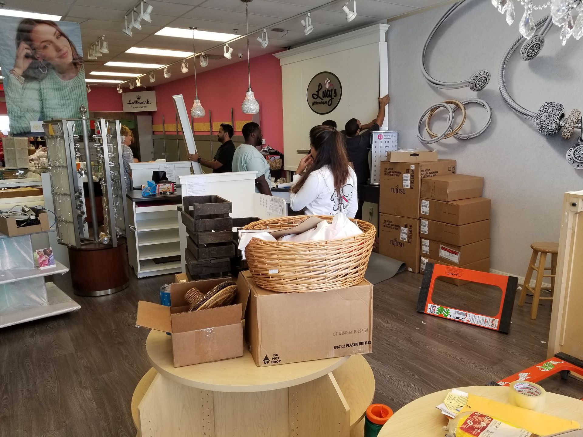 People setting up a shop. Boxes and merchandise are in the store. Pink walls and light fixture with happy client