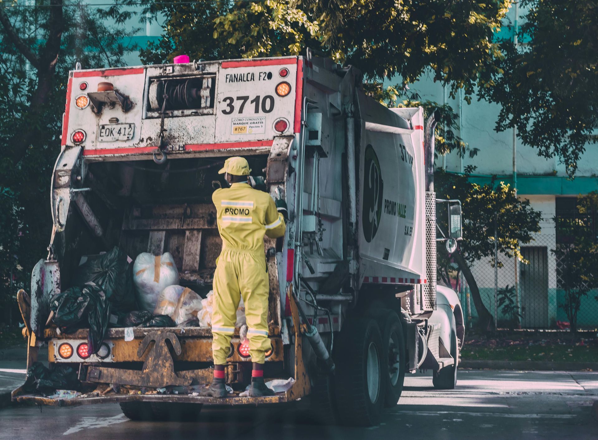 A man in a yellow jumpsuit is standing in front of a garbage truck.