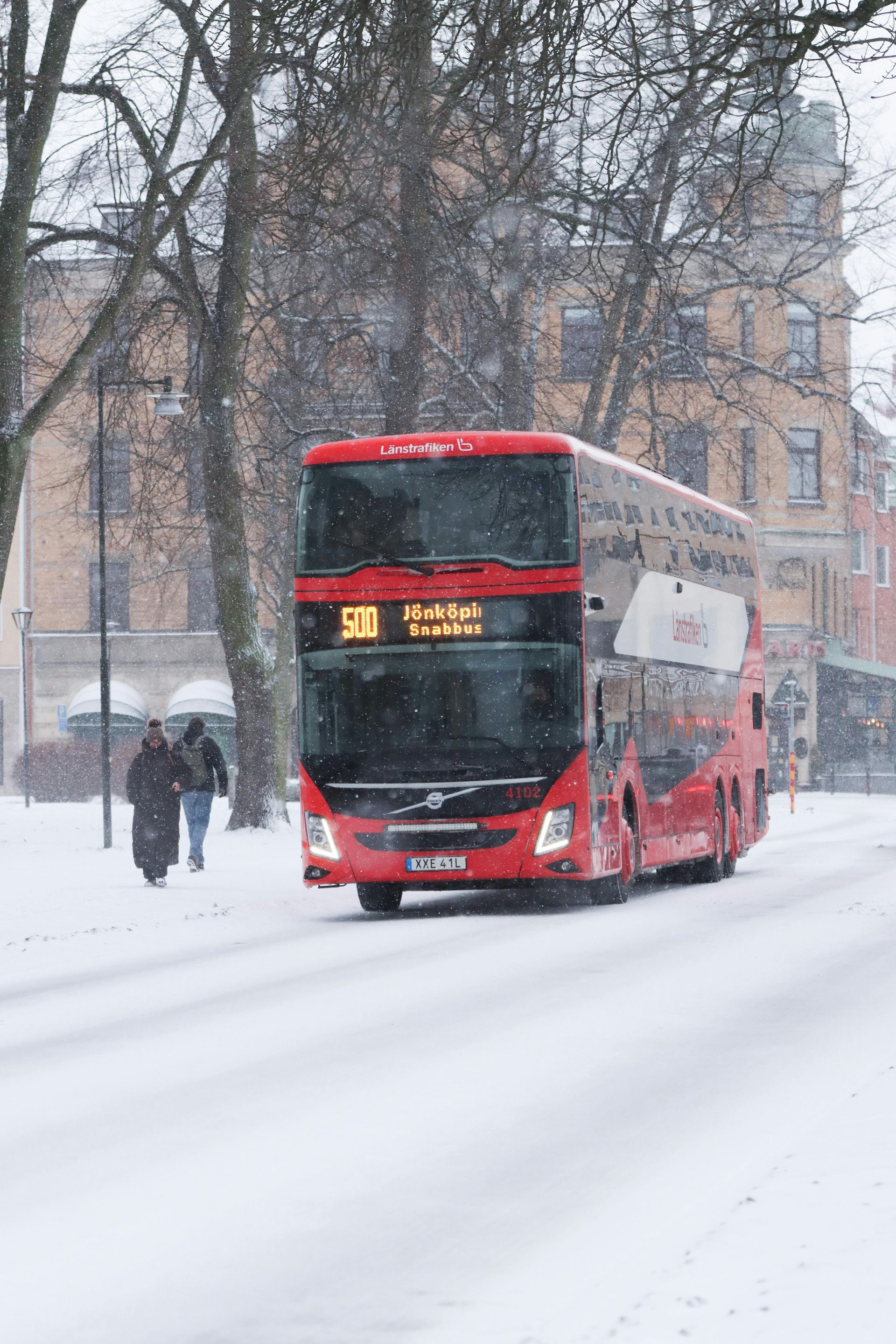 A red double decker bus is driving down a snowy street.