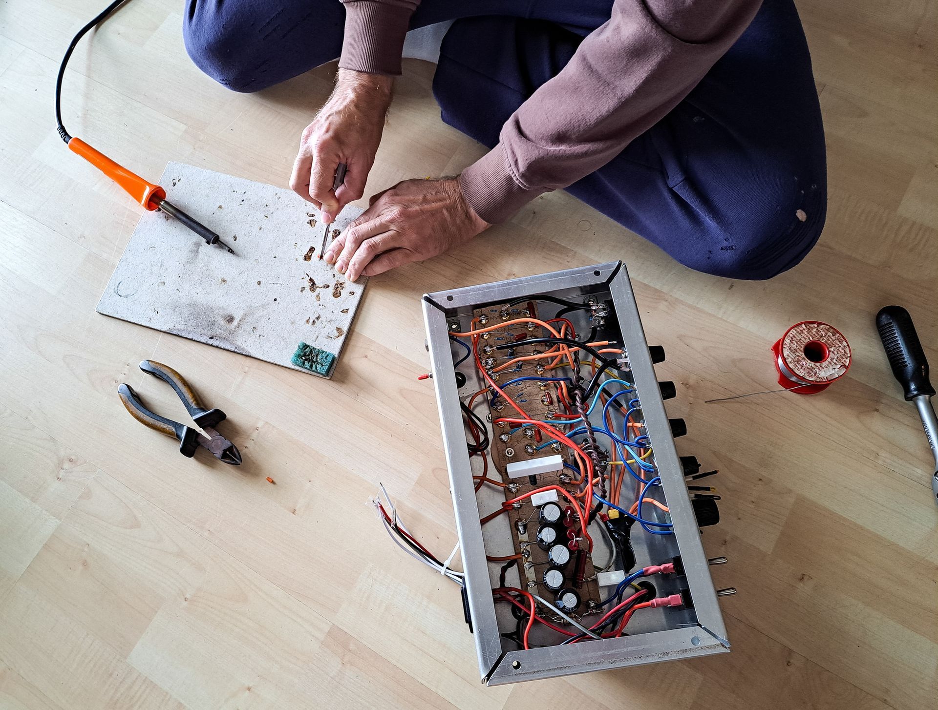 A person is kneeling on the floor working on an electronic device.