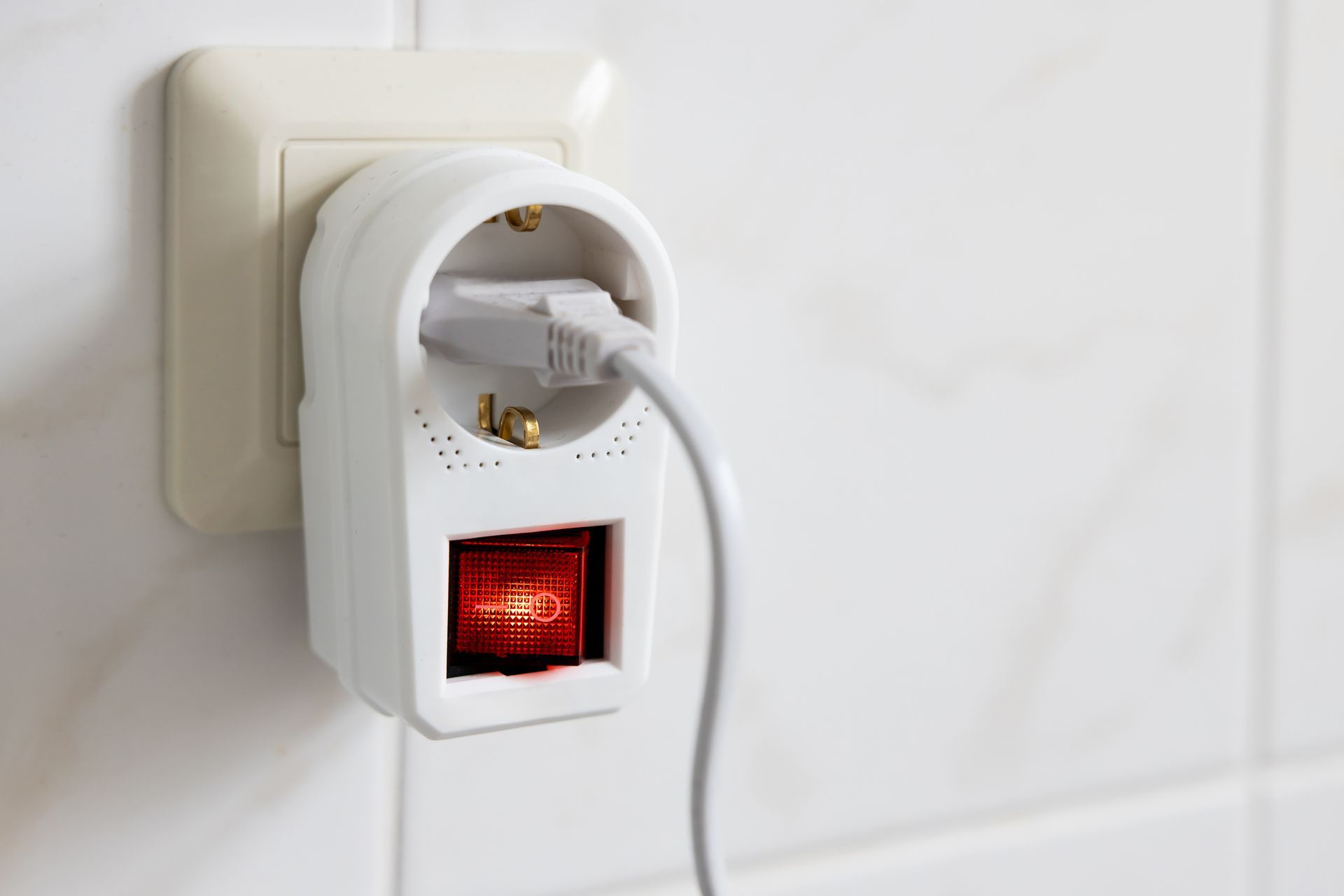 A plug with a red light on it is plugged into a wall socket.
