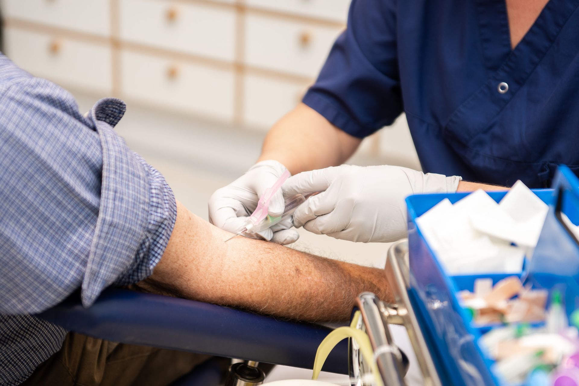 En läkare tar blodprov från en patients arm. Händer i handskar, steril miljö, blå skrubbkläder.