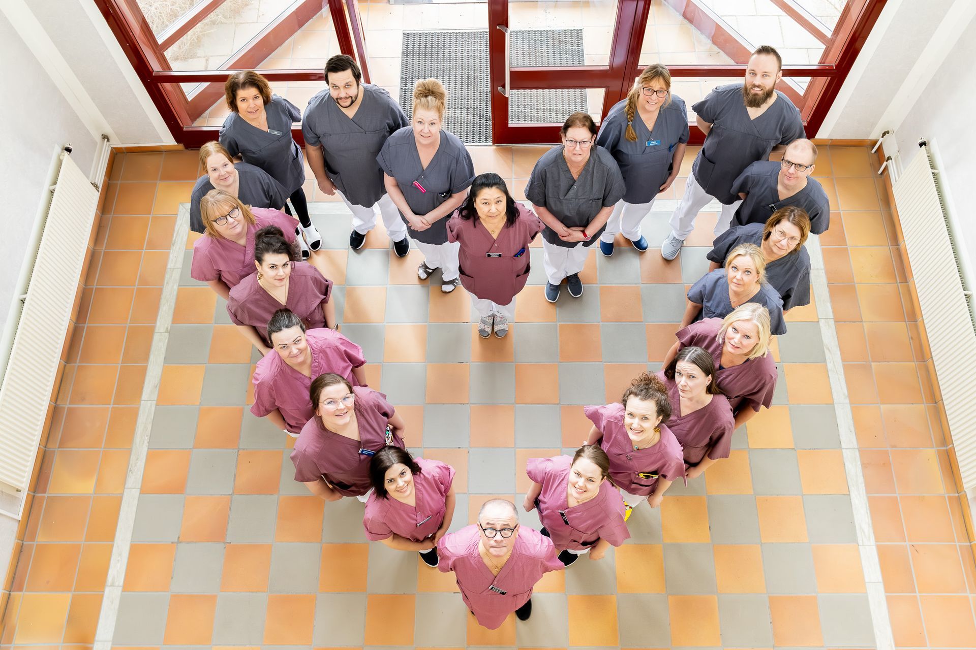 Sjukvårdspersonal i scrubs formar ett hjärta och tittar upp in i kameran.