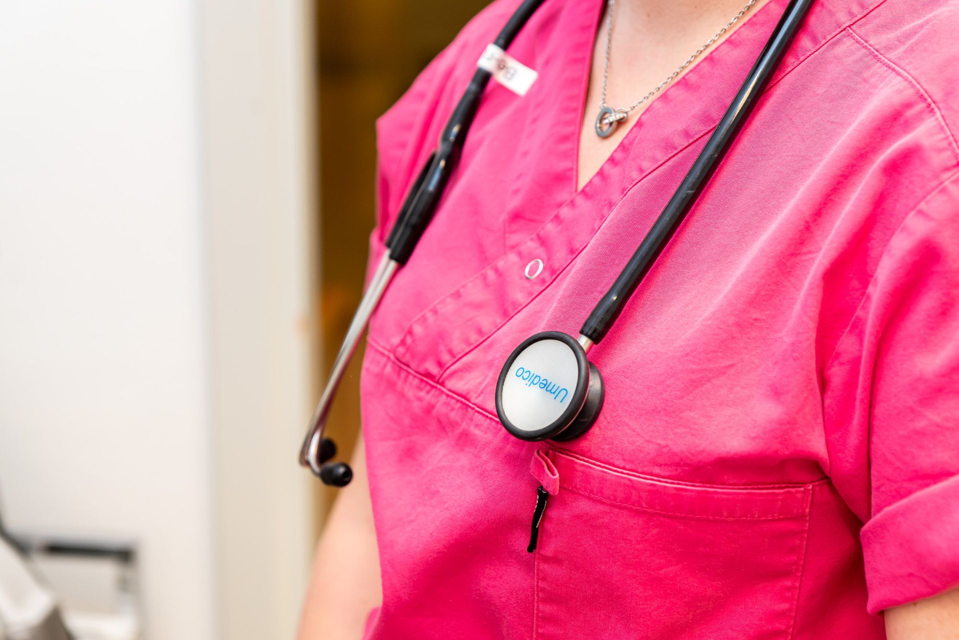 Sjuksköterska i rosa scrubs med ett stetoskop runt halsen.