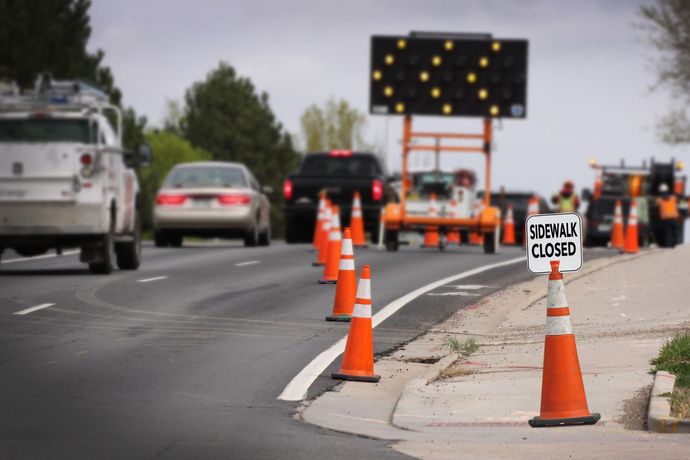 Roadwork lane closure with orange cones, road sign, and traffic on a city street