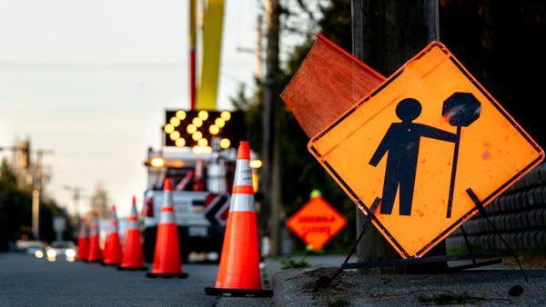Orange roadwork warning signs and traffic cones lining a street with a blurred barrier in the background
