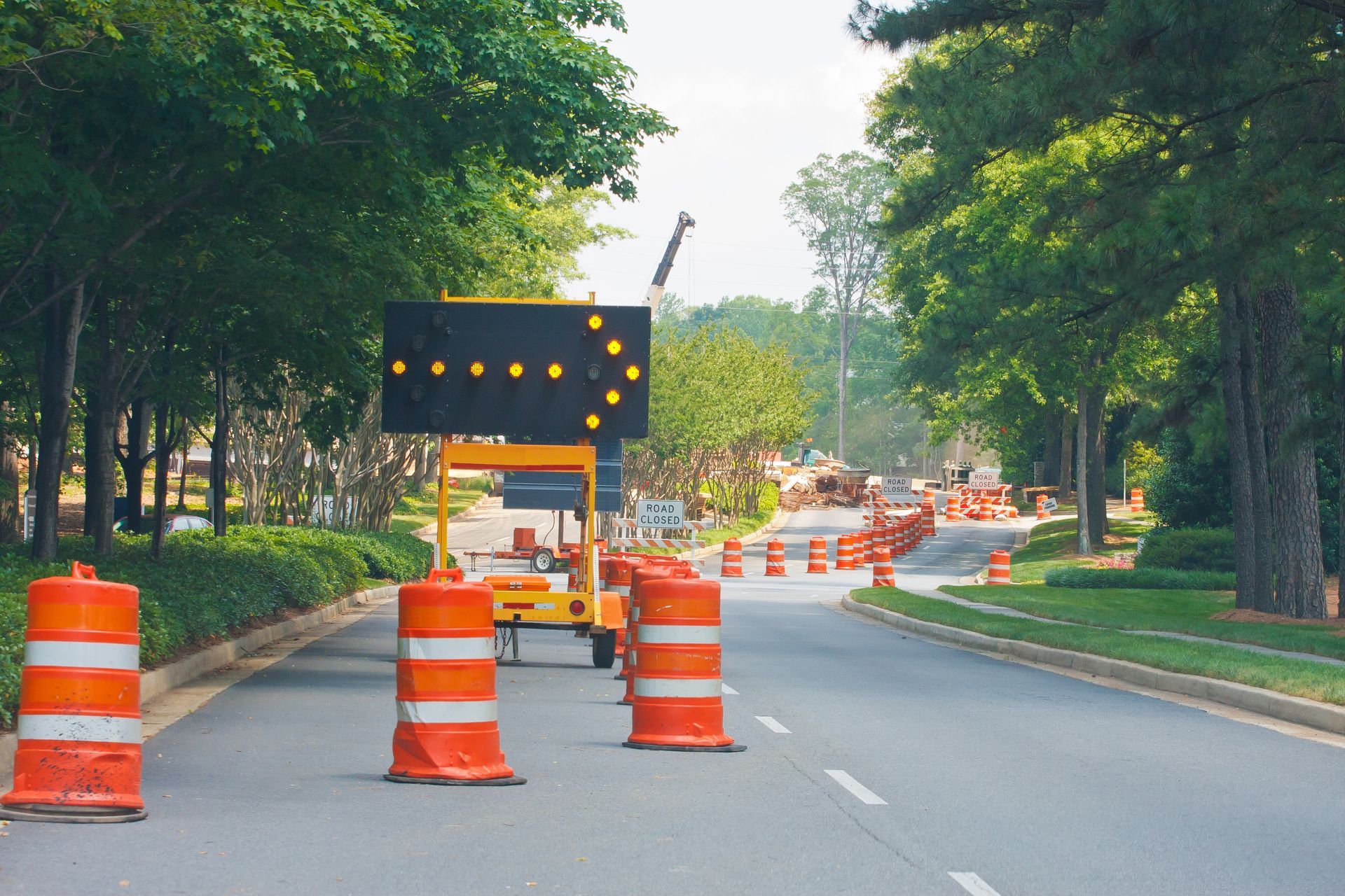 Road blocked by orange barrels and construction sign on a tree-lined street.