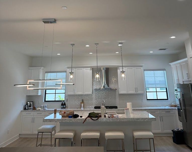 Modern white kitchen with island, pendant lights, and stainless steel appliances.