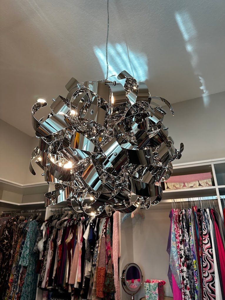 A chandelier is hanging from the ceiling in a closet filled with clothes.