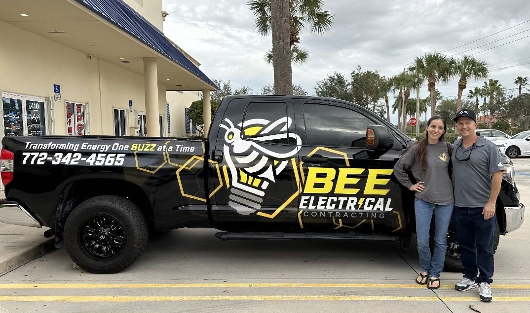 A man and a woman are standing in front of a bee electrical truck.