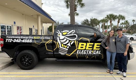A man and a woman are standing in front of a bee electrical truck.