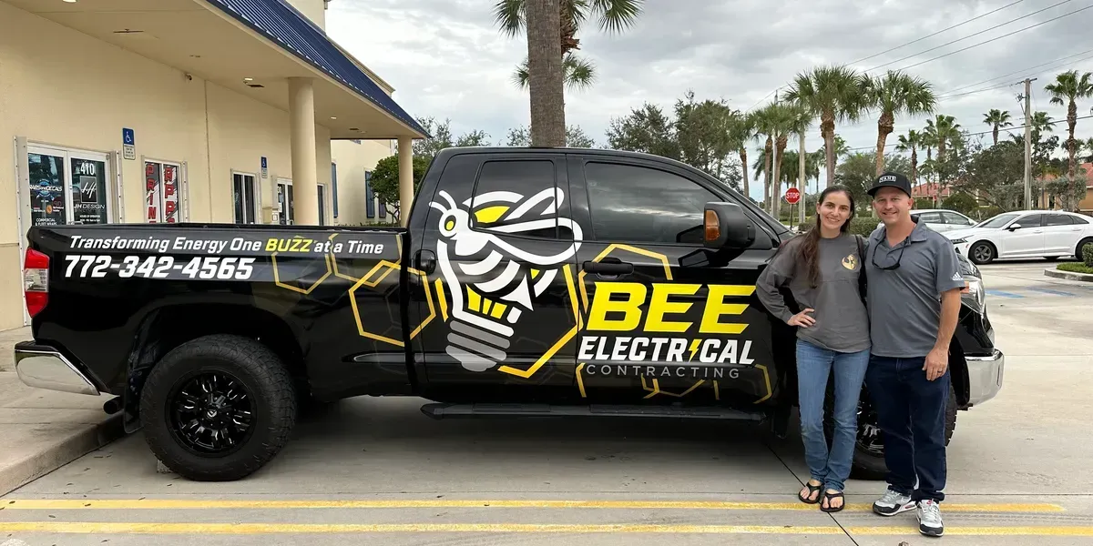 A man and a woman are standing in front of a bee electrical truck.