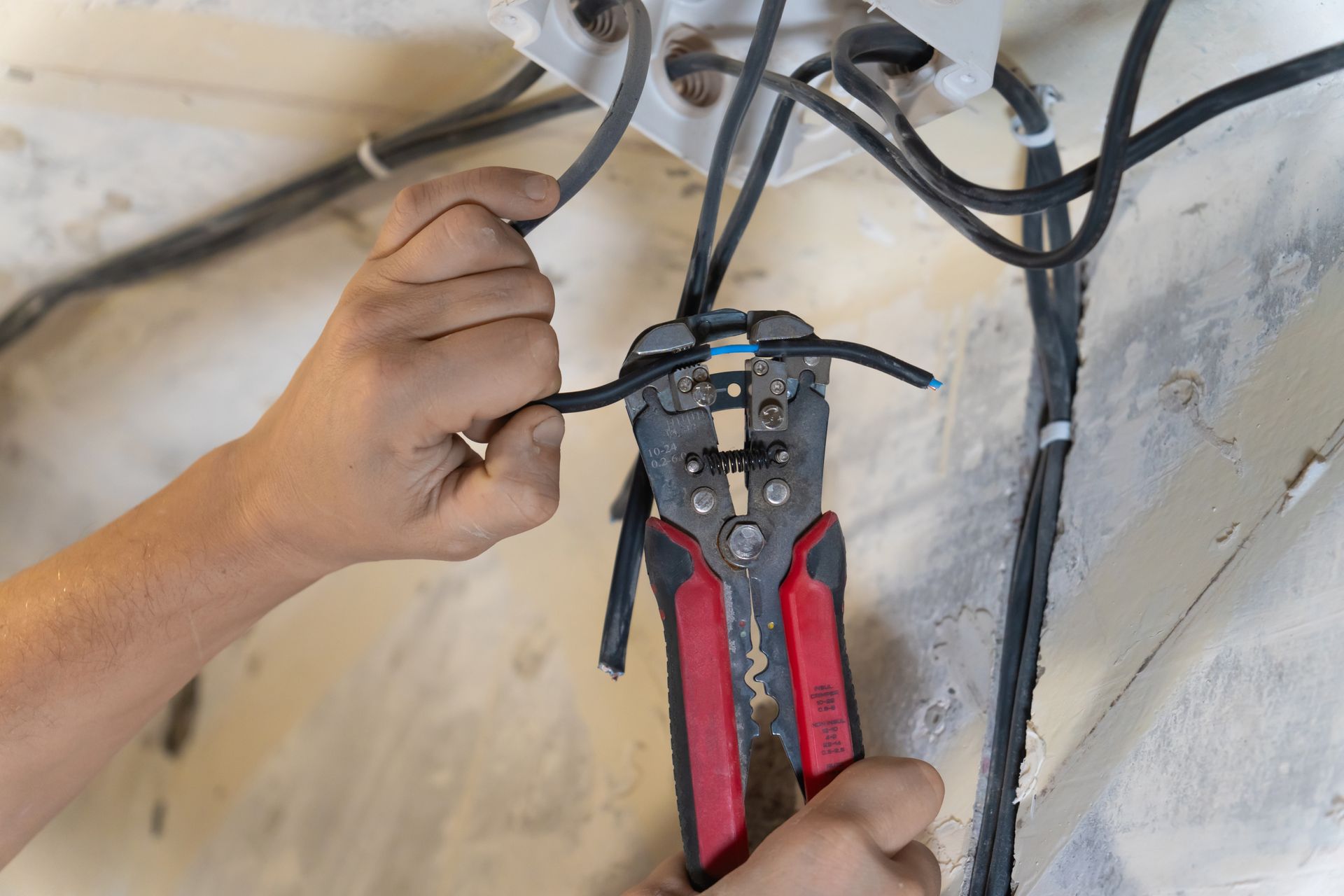 Person using wire strippers to work on electrical wires near a wall.