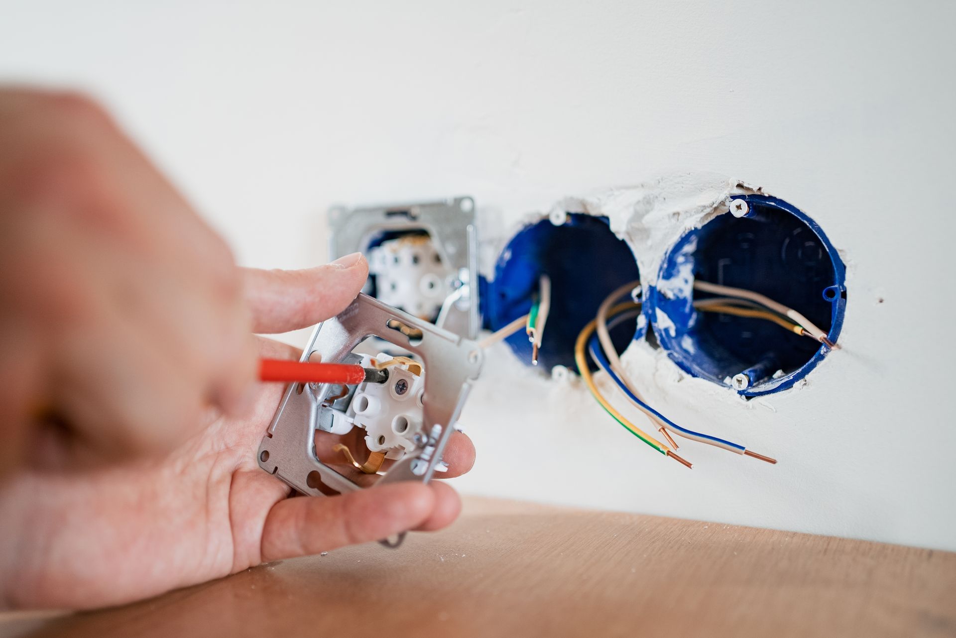 Hand wiring an electrical outlet; red screwdriver, wires, and blue electrical boxes.