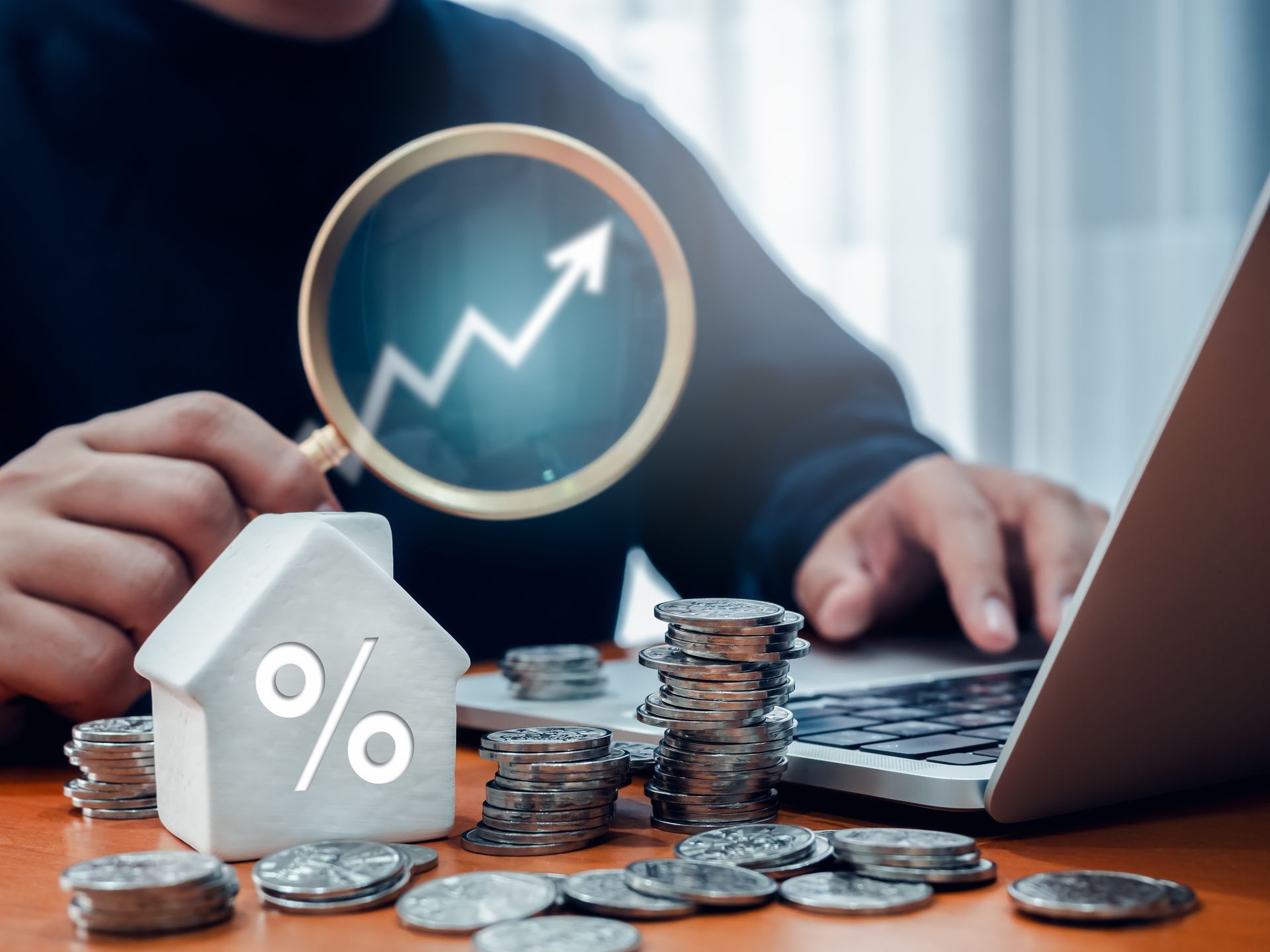 A man is using a laptop and looking at a house with a magnifying glass.