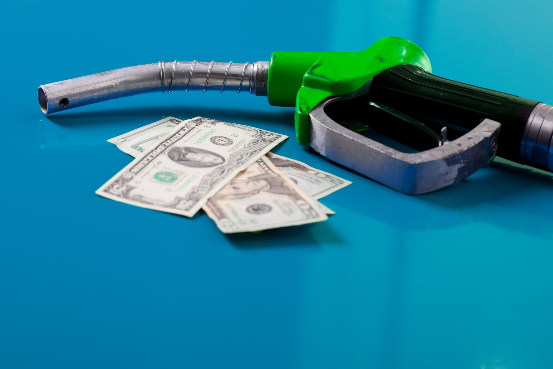 A gas pump and some money on a blue surface.