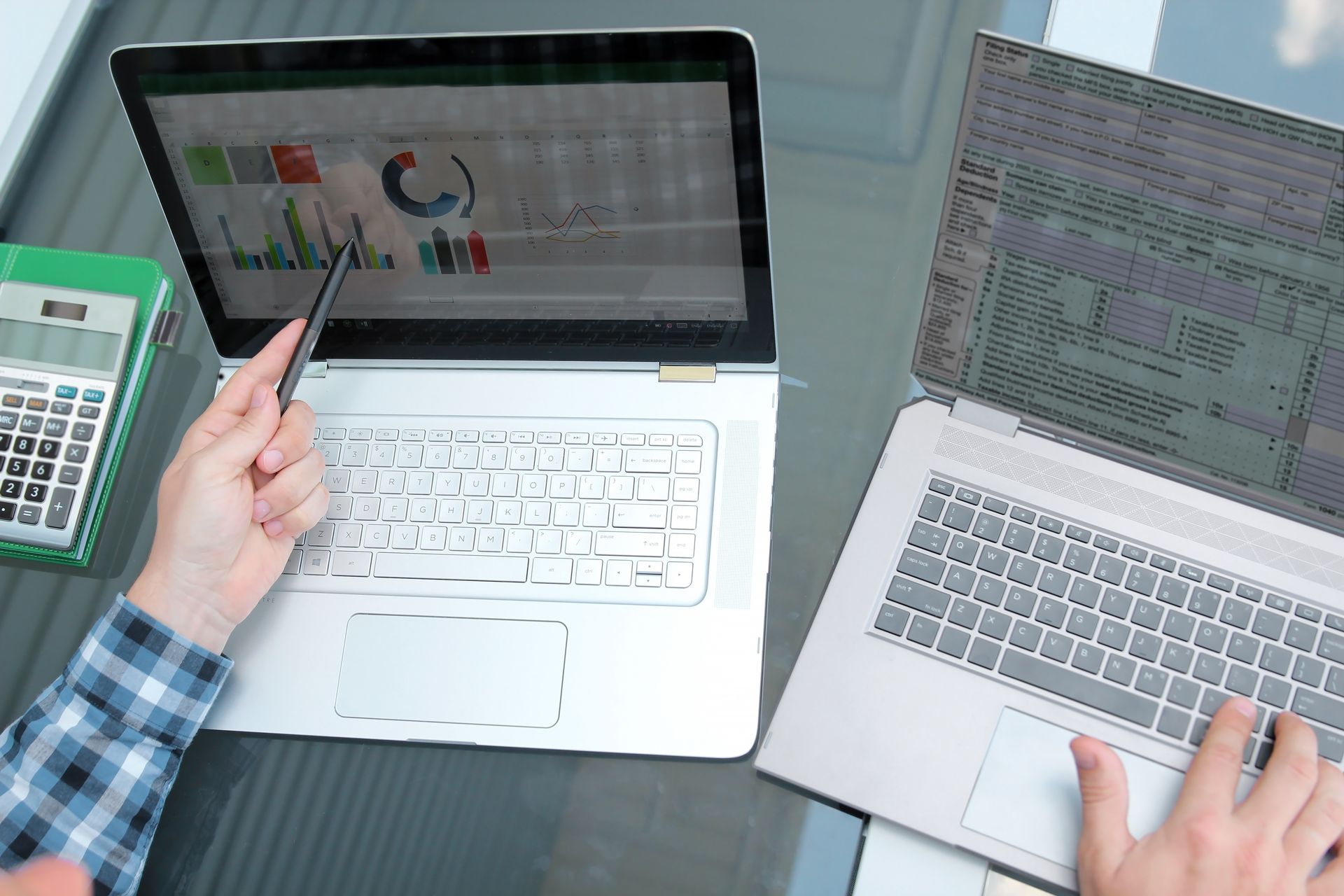 Two people are using laptops and a calculator on a table.