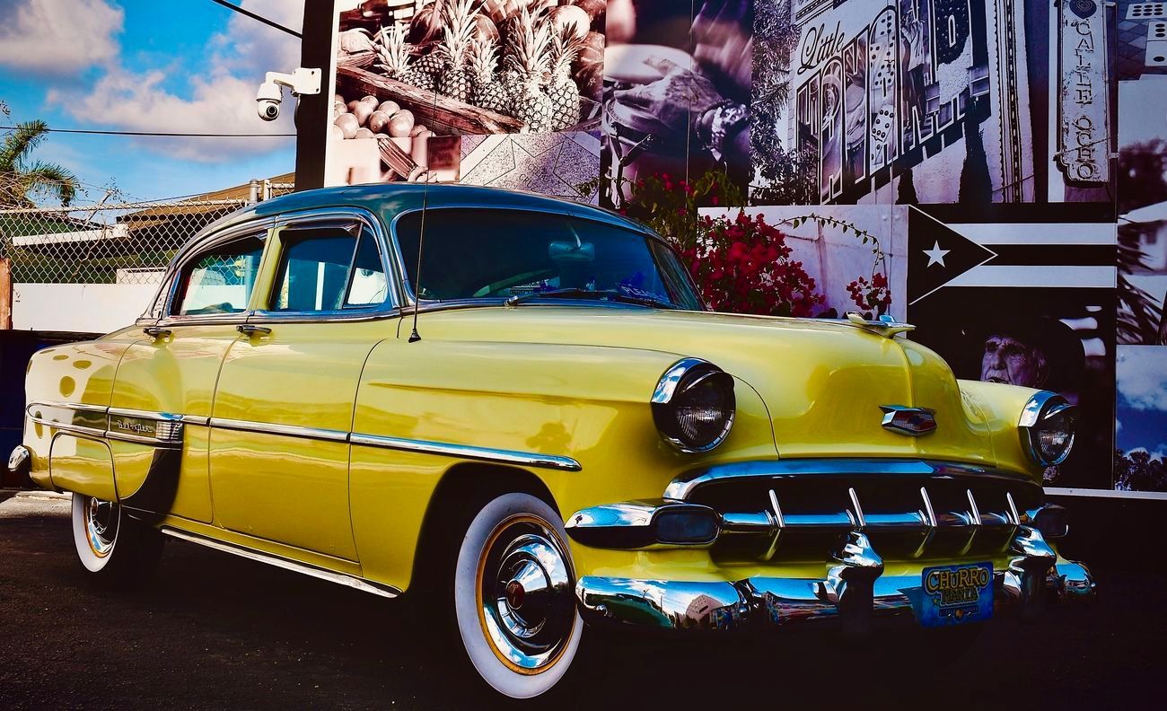 Yellow classic car parked in front of a mural with a Cuban flag.