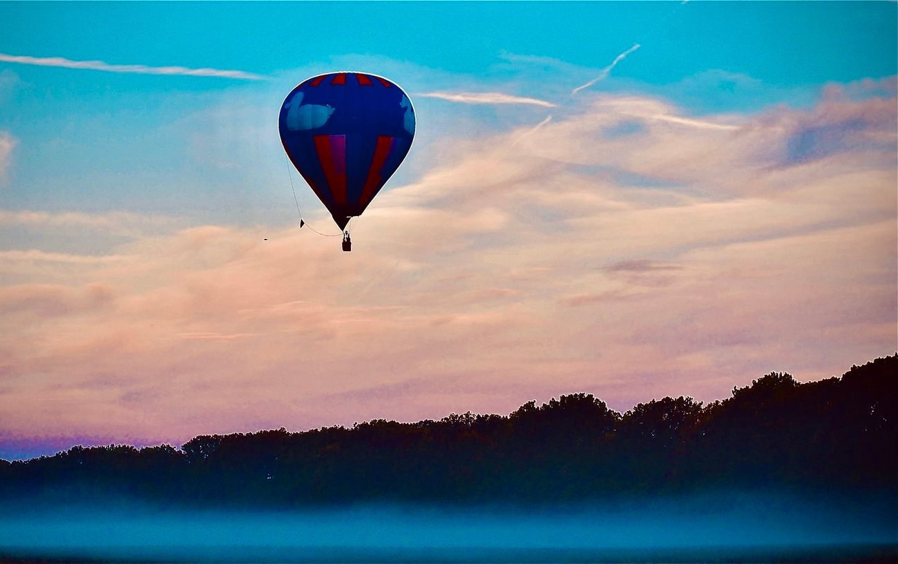Hot air balloon with red and blue stripes against a colorful sunset sky.