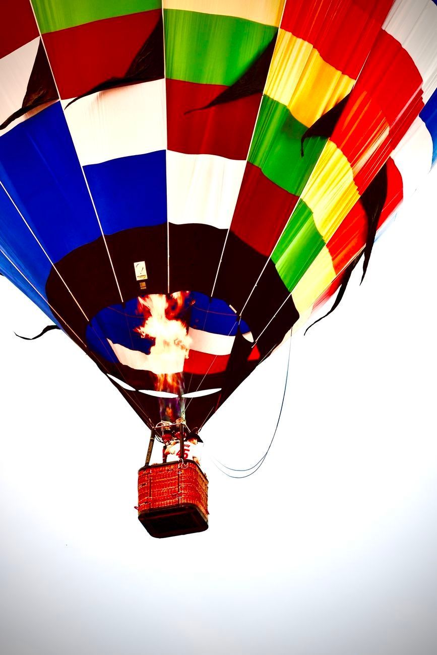 Colorful hot air balloon with flames in the basket, against a white sky.