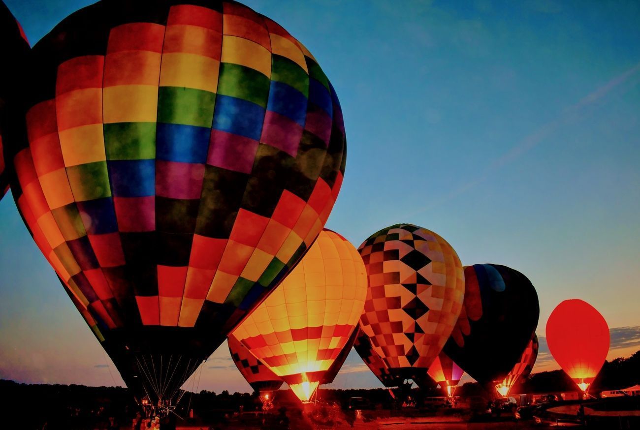 Hot air balloons glowing at dusk, colorful against a blue sky.