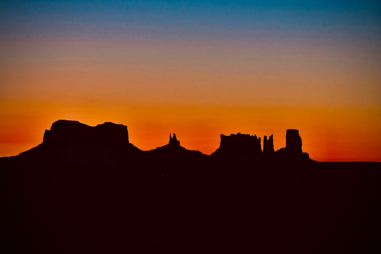 Silhouetted rock formations against an orange and blue sunset.