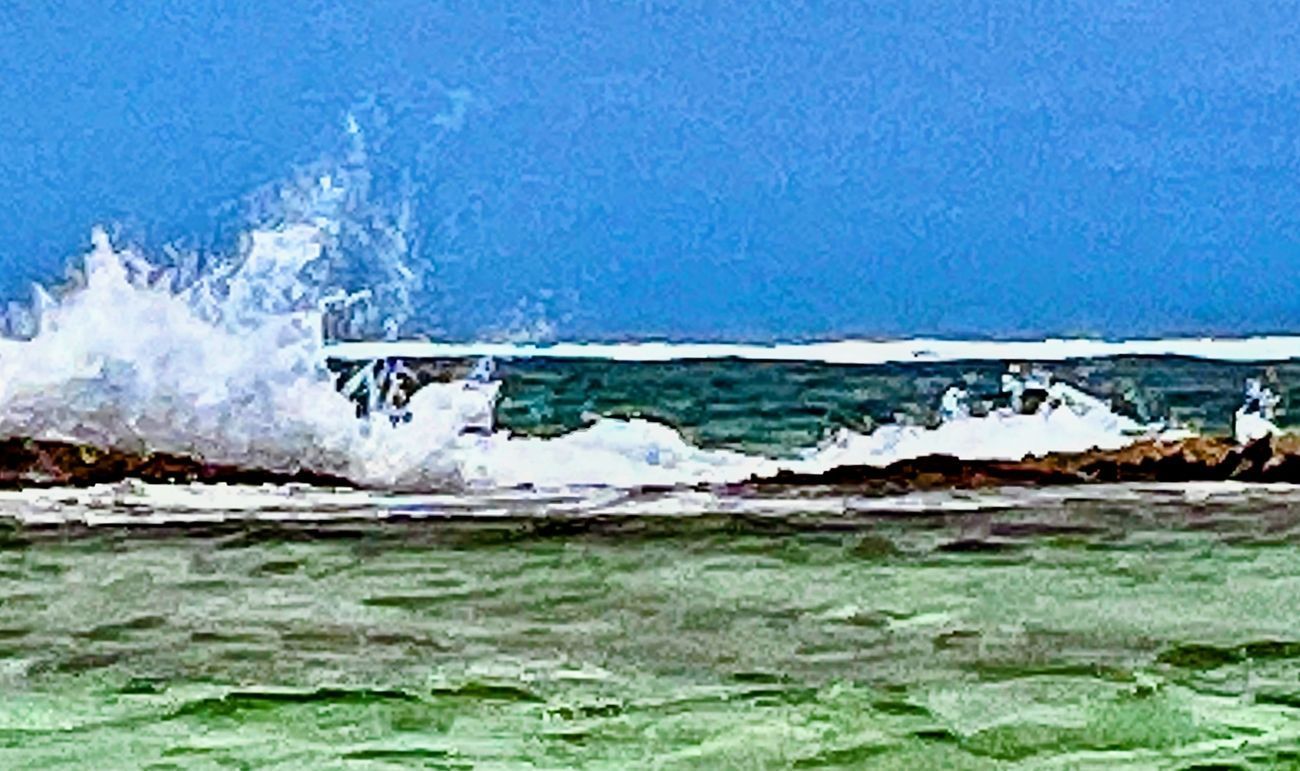 Ocean waves crashing on a rocky shore, turquoise water, and a bright blue sky.