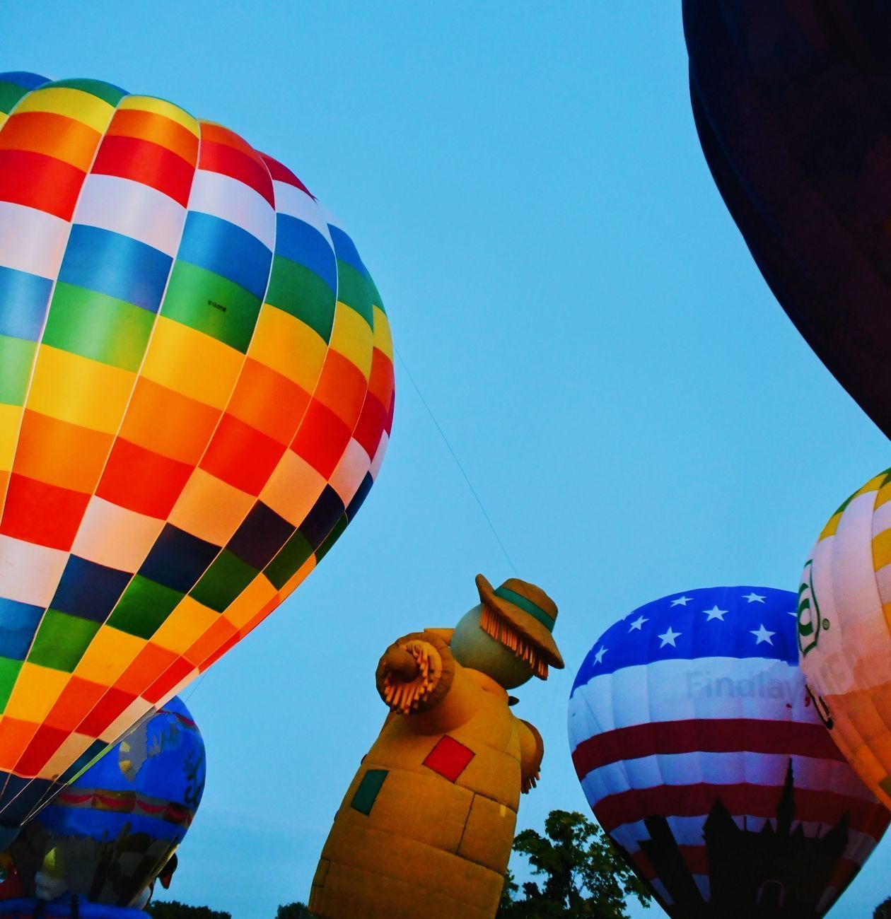 Hot air balloons with colorful patterns fill the sky, including one shaped like a scarecrow.