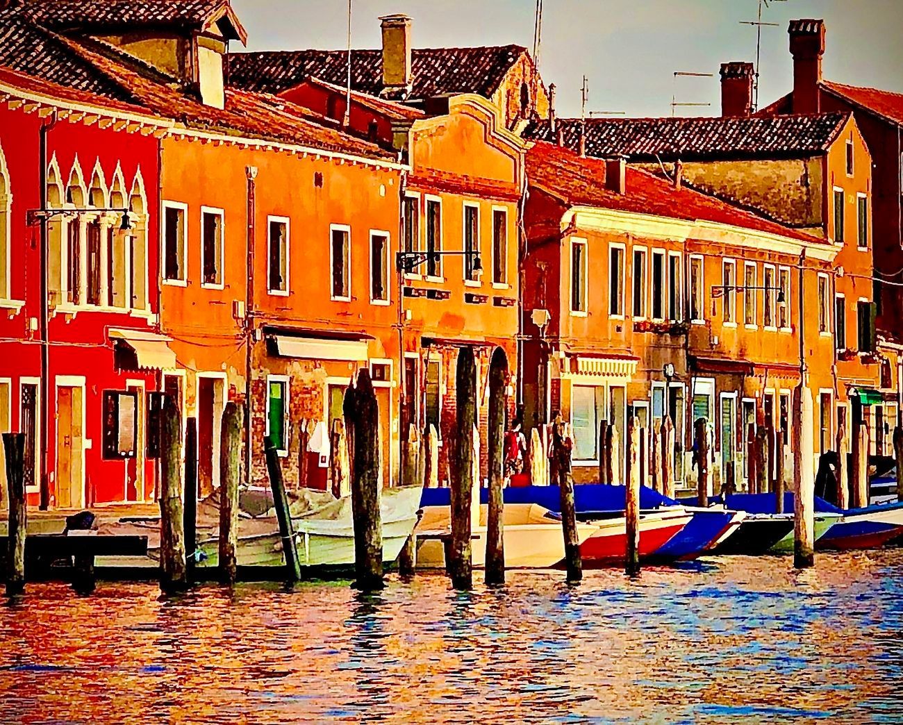 Colorful buildings line a canal with boats and wooden posts.