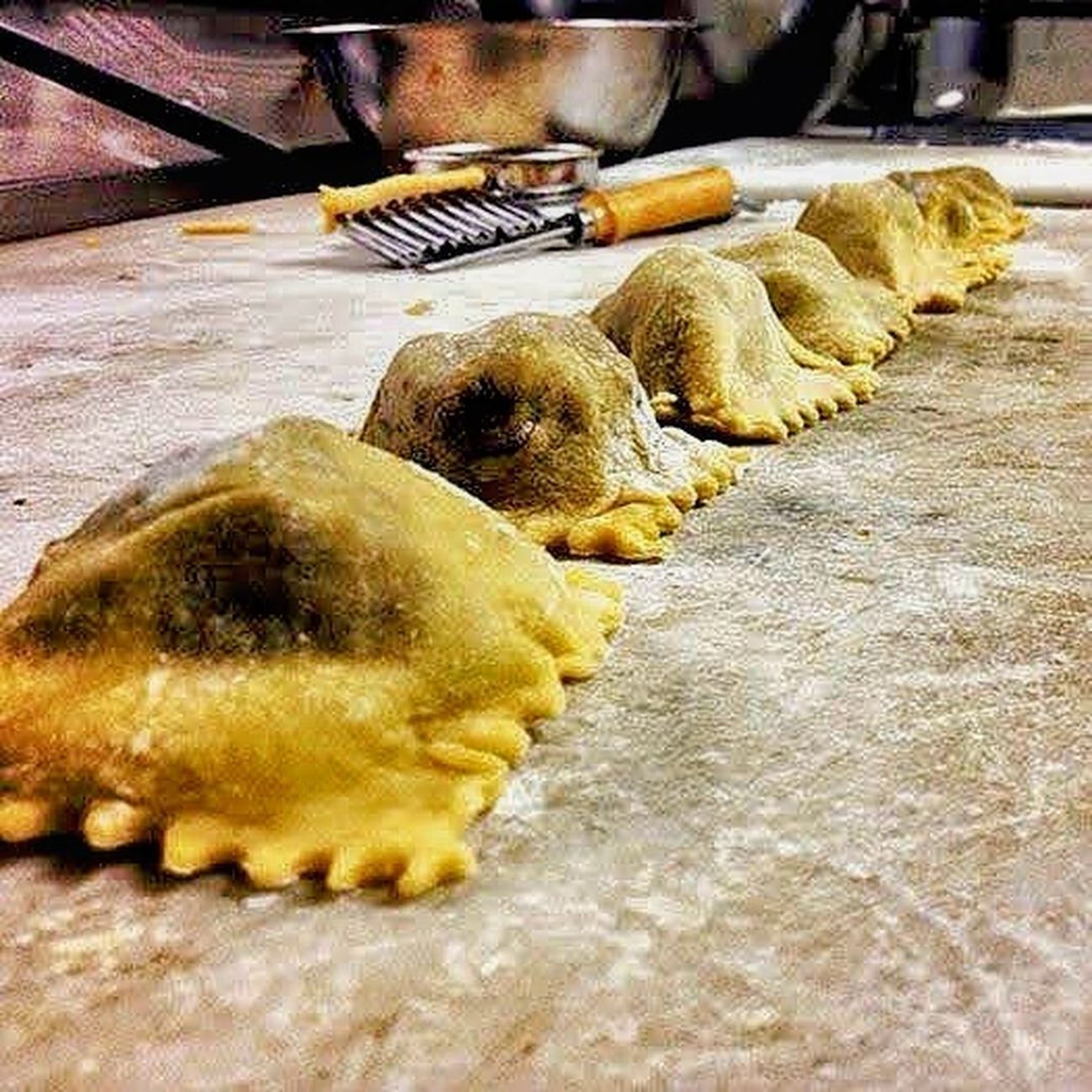 Row of ravioli on a floured surface, with pasta cutter and bowl in background.