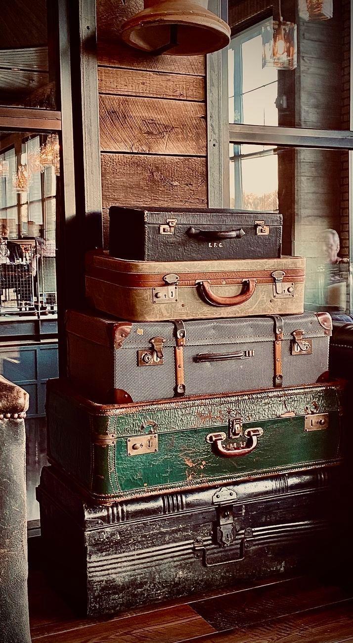 Stack of vintage suitcases, varying colors and sizes, in a rustic setting with wooden walls.